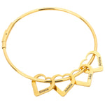 A gold-colored bracelet with multiple heart-shaped charms, each with a different name inscribed on it, on a white background.